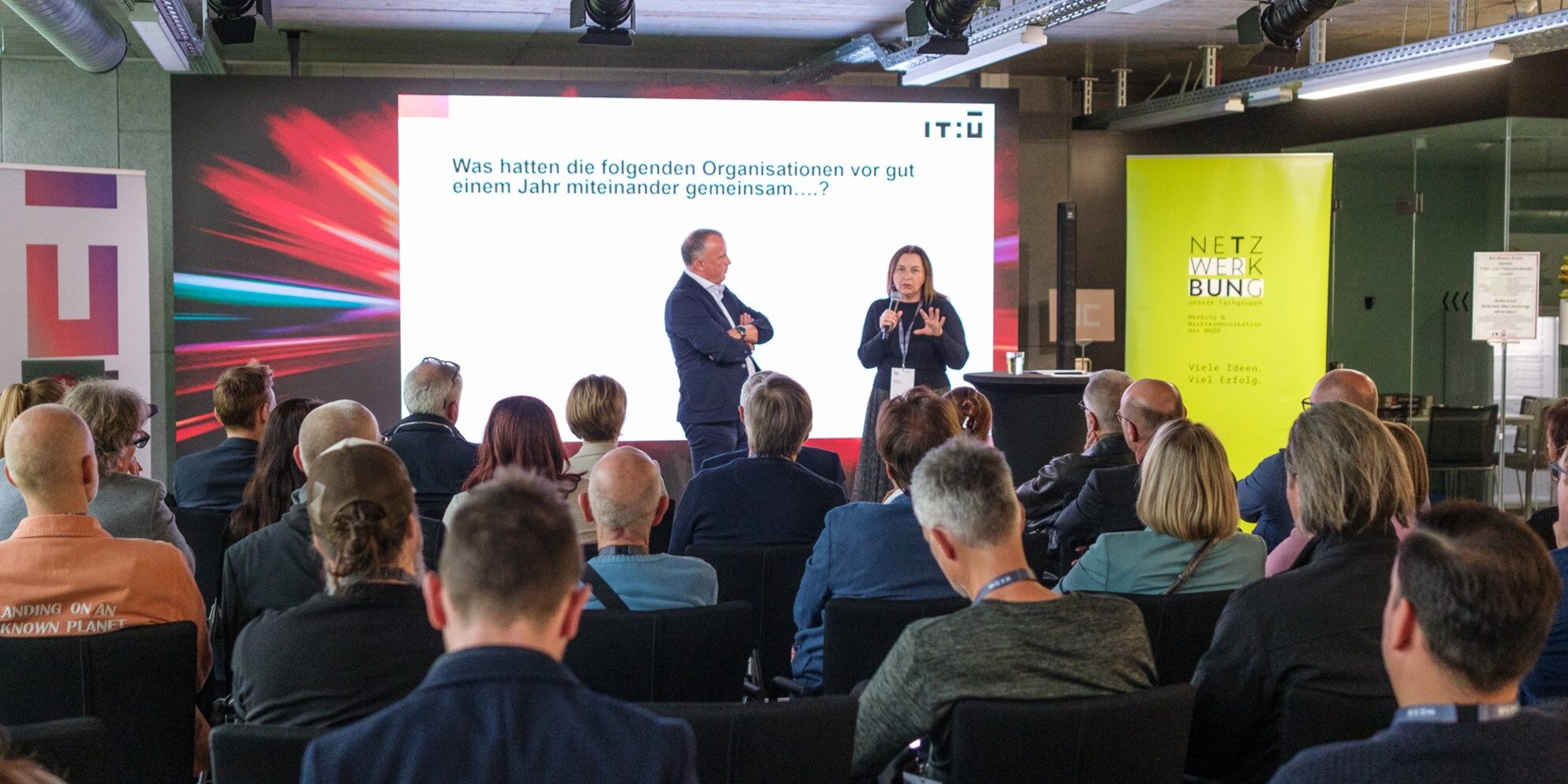 Vortrag vor Publikum bei einer Netzwerkveranstaltung mit Präsentation im Hintergrund