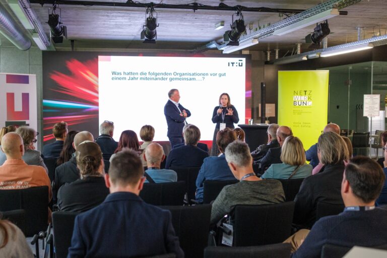 Vortrag vor Publikum bei einer Netzwerkveranstaltung mit Präsentation im Hintergrund
