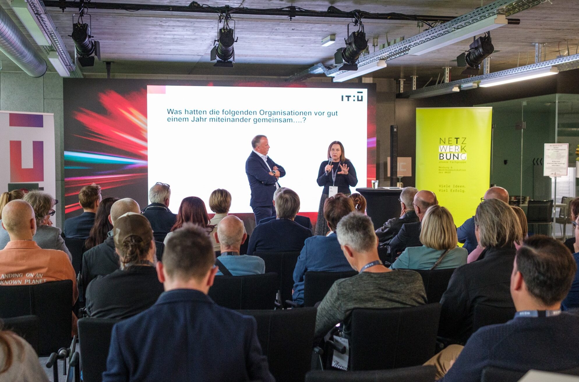 Vortrag vor Publikum bei einer Netzwerkveranstaltung mit Präsentation im Hintergrund