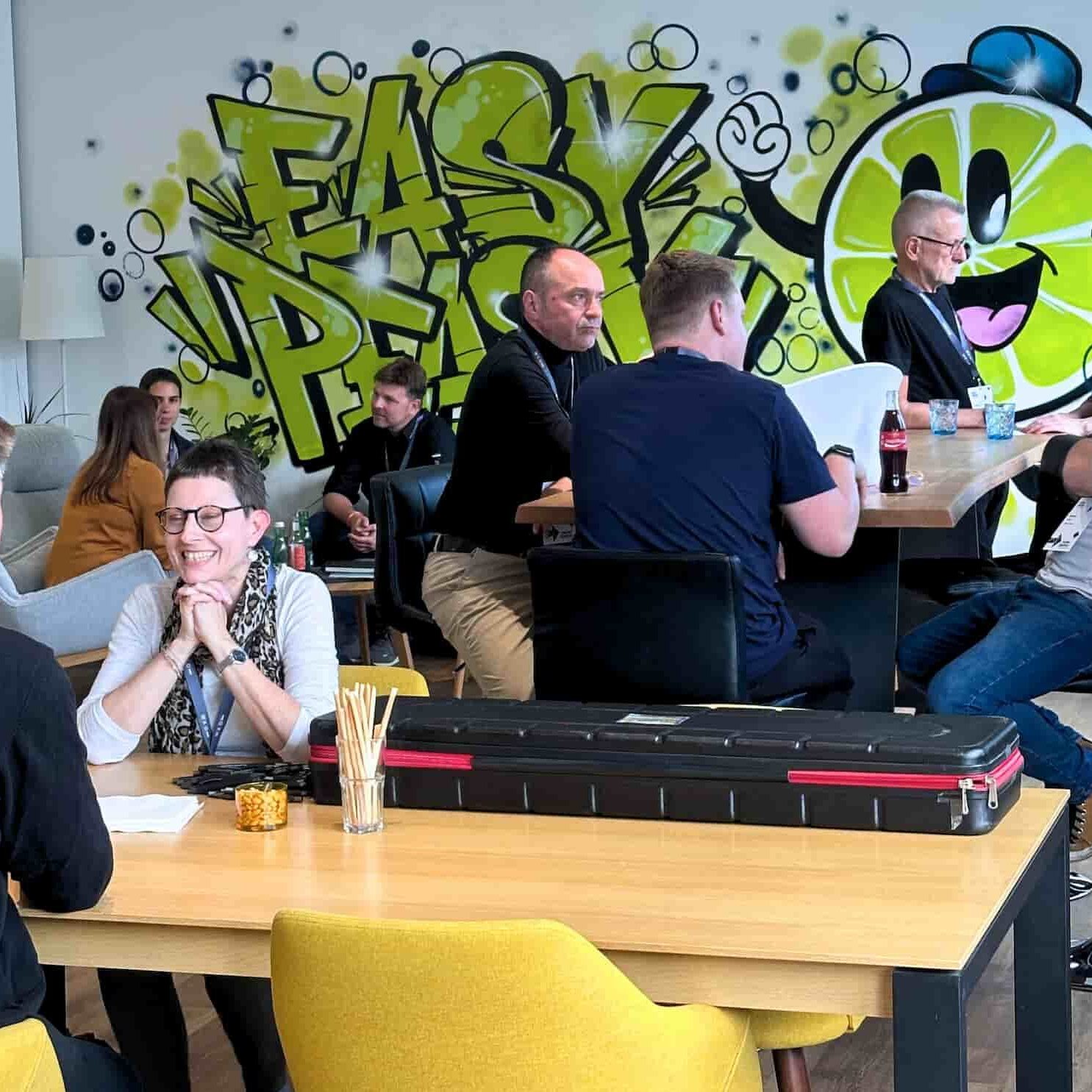 Menschen im entspannten Gespräch, im Hintergrund ein Graffitti "Easy Peasy" mit einem Zitronen-Smiley