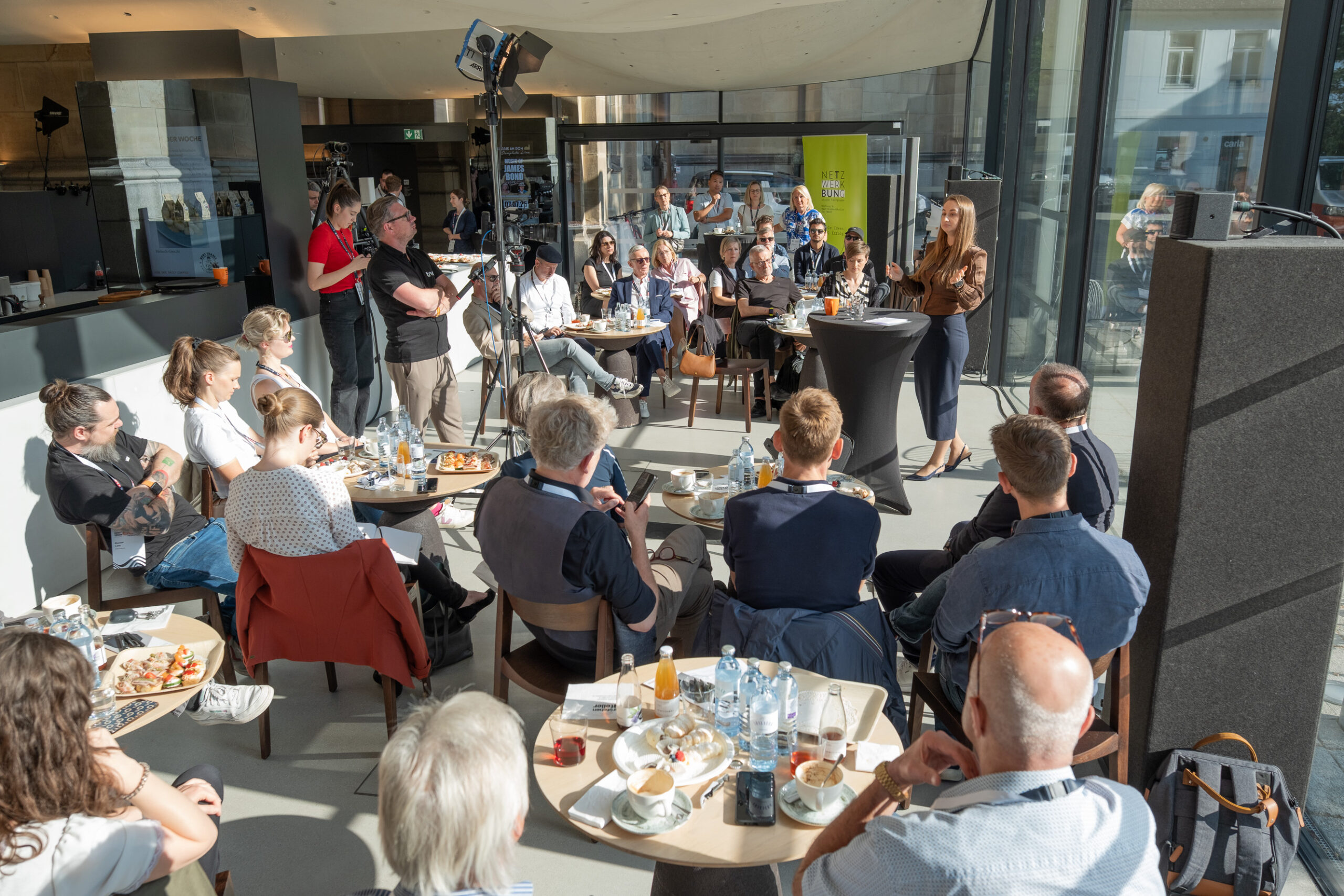 Frau spricht vor Publikum in modernem Café bei Tageslicht