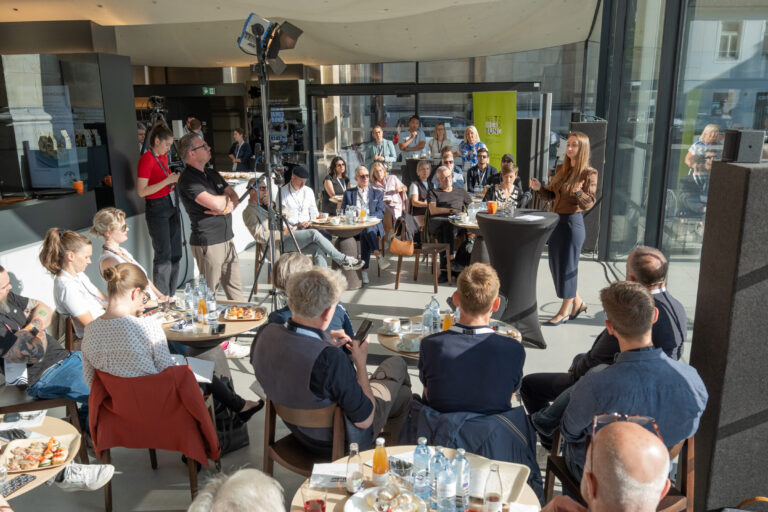 Frau spricht vor Publikum in modernem Café bei Tageslicht