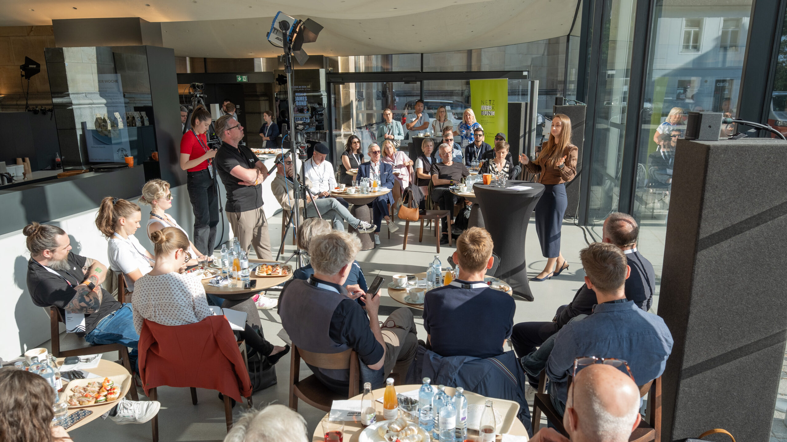 Frau spricht vor Publikum in modernem Café bei Tageslicht