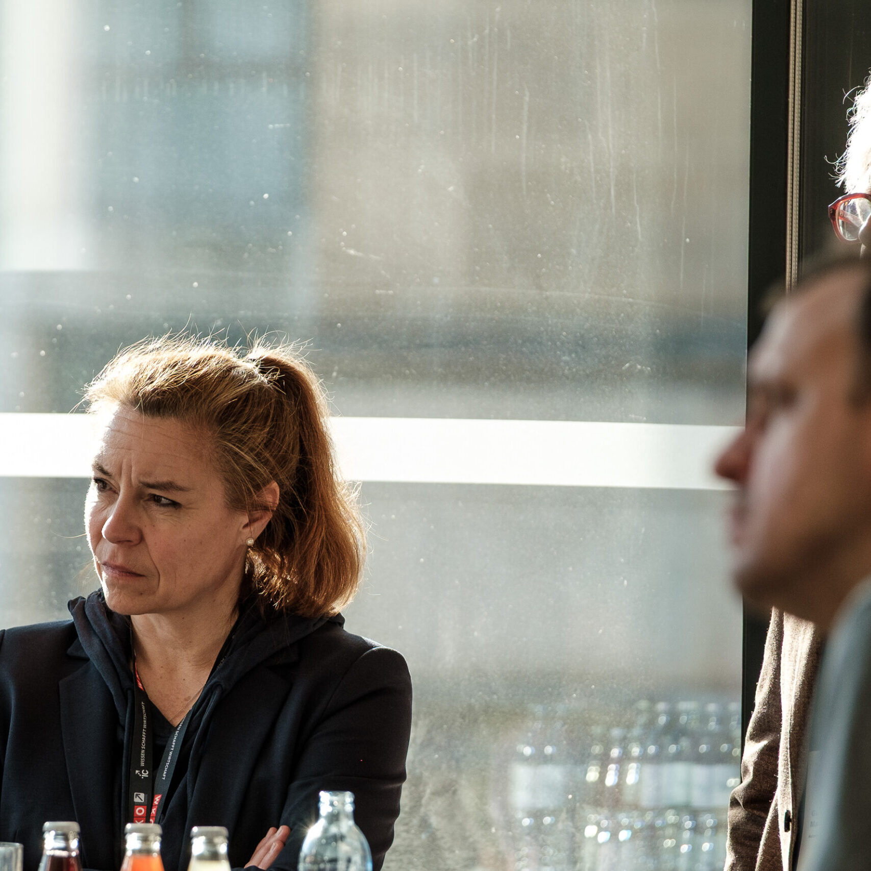 Eine Denkfrühstück-Teilnehmerin hört aufmerksam zu; zwei weitere Teilnehmer sind am Rand des Bildes zu sehen