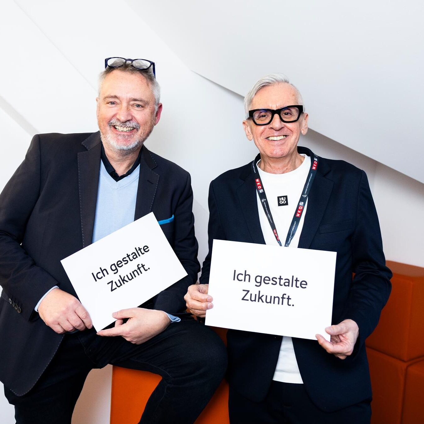 Zwei lächelnde Männer stehen mit weißen "Ich gestalte Zukunft"-Schildern im Büro