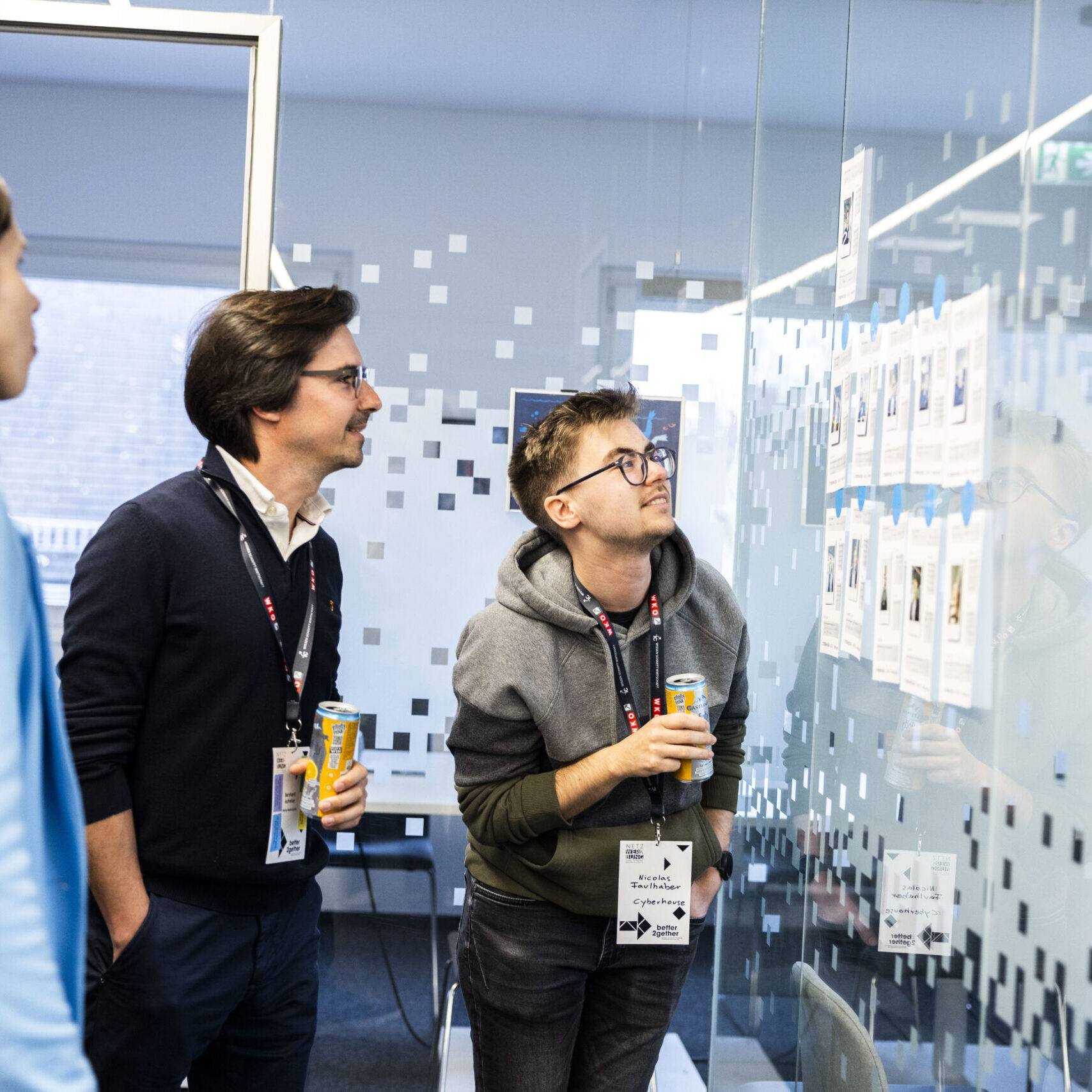 Zwei Männer und eine Frau blicken interessiert auf eine Glaswand mit Dokumenten