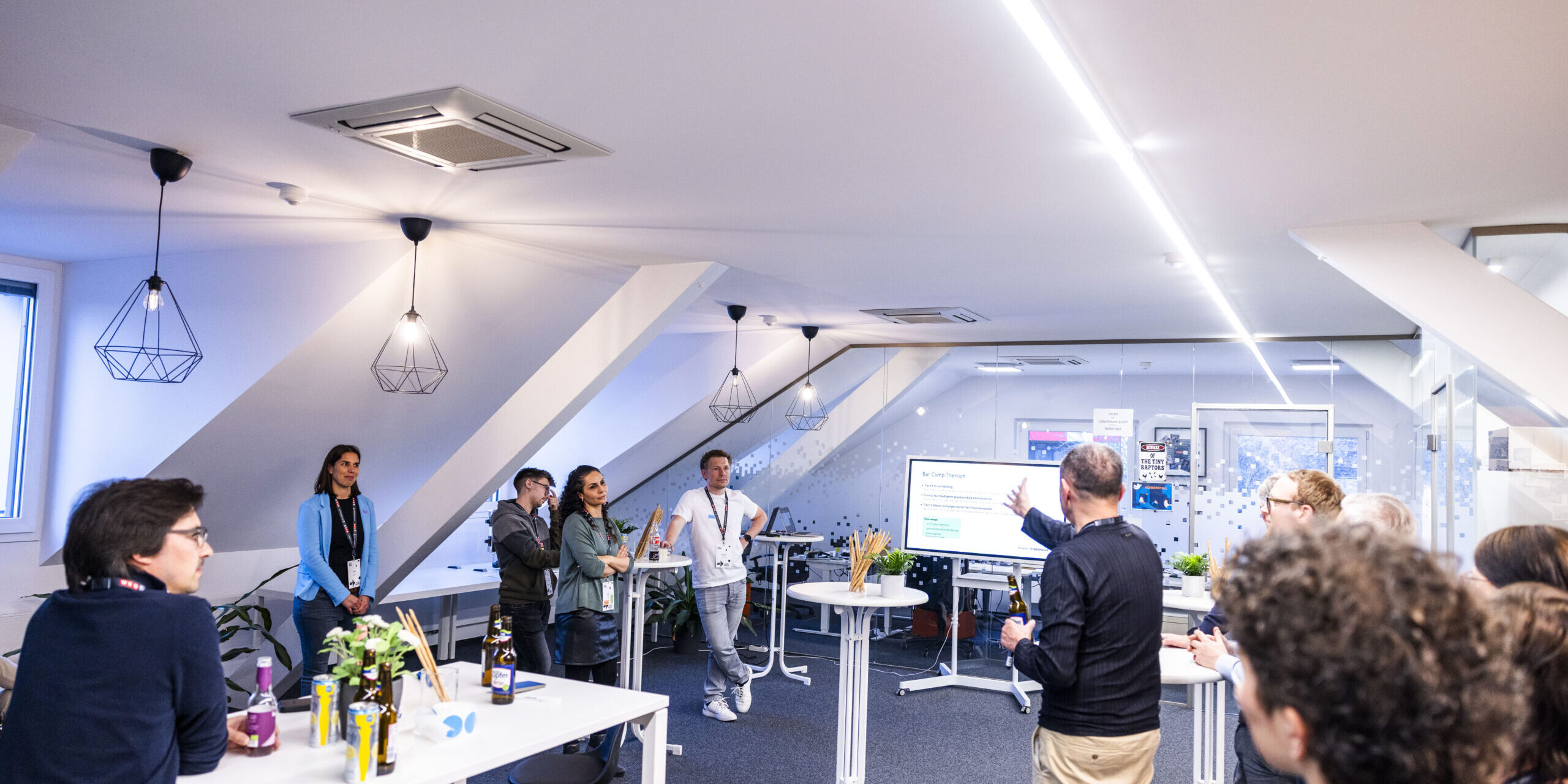 Cyberhouse-Büroräumlichkeiten mit einem Bildschirm, Stehtischen und Gästen