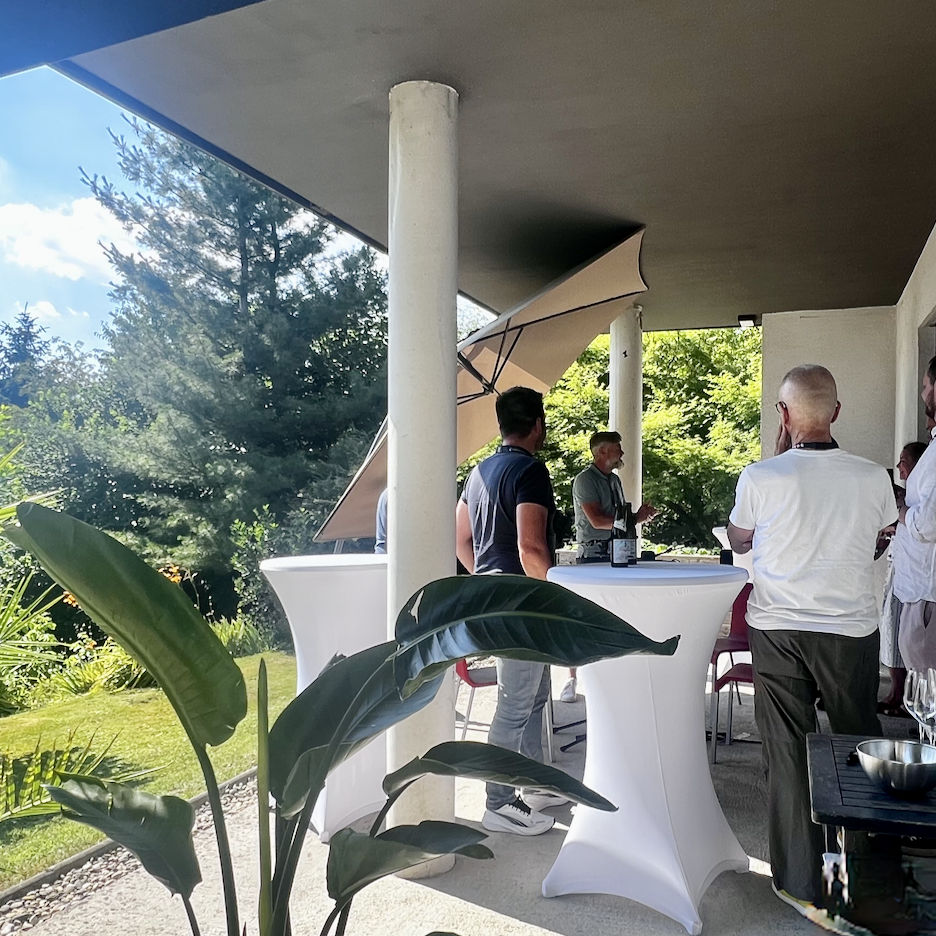 Headergrafik mit Personen im Gespräch an Stehtischen auf einer Gartenterrasse.