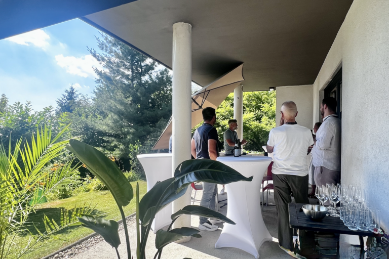 Personen im Gespräch an Stehtischen auf einer Gartenterrasse.