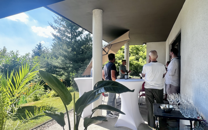 Personen im Gespräch an Stehtischen auf einer Gartenterrasse.