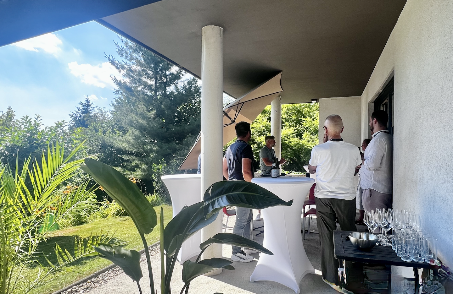 Personen im Gespräch an Stehtischen auf einer Gartenterrasse.